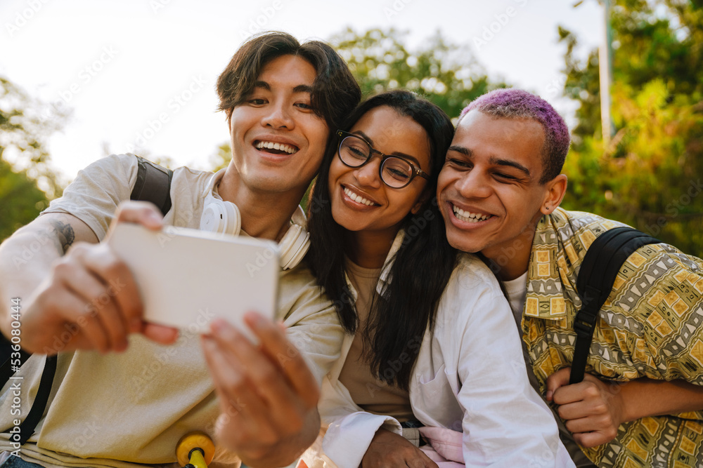 Fototapeta premium Three multiracial friends taking selfie photo in skate park