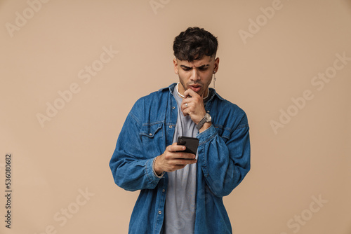 Brunette young man wearing shirt frowning and using cellphone © Drobot Dean