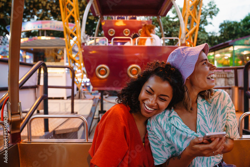 Young multiracial women using cellphone while riding on ferris wheel