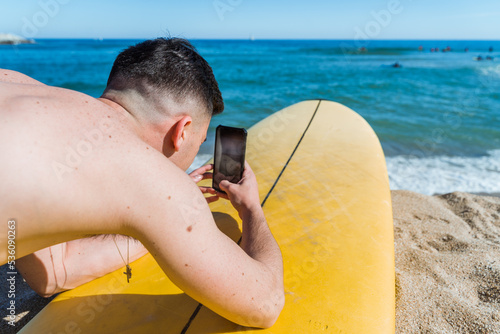 Surfer taking photo on smartphone on beach