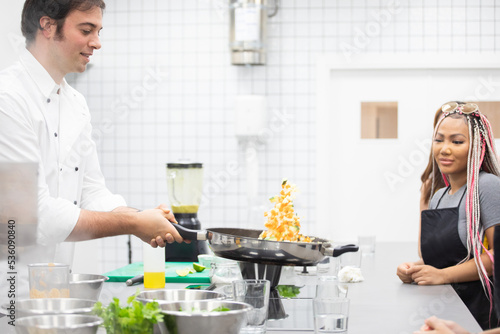 Professional chef demonstrating technique of tossing ingredients on pan to multi ethnic students at cooking workshop
