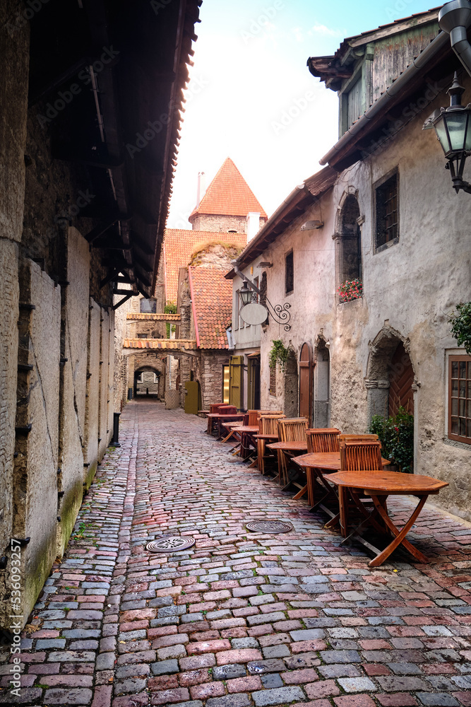 Catherine Lane in Tallinn, Estonia, on a rainy day. Wet tables and chairs of outdoor cafe. Ancient cobbled lane in historic district of Old Town, Tallinn, Estonia