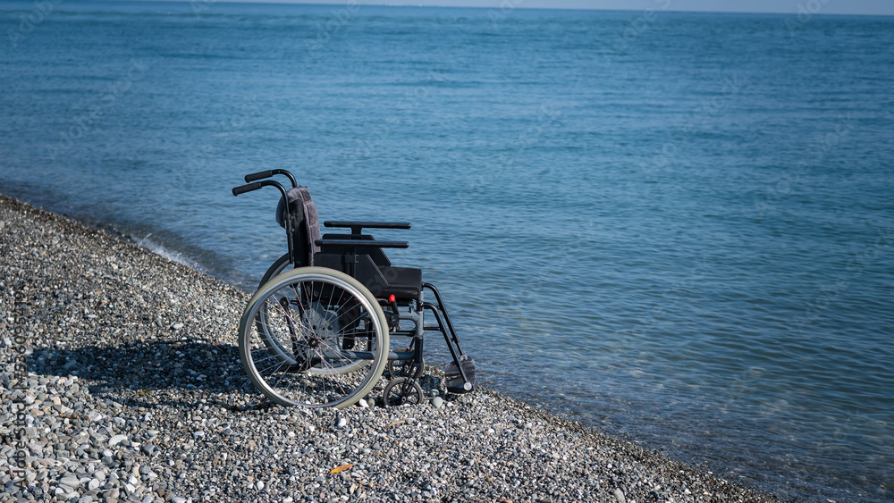 Fototapeta premium An empty wheelchair on a rocky seashore.