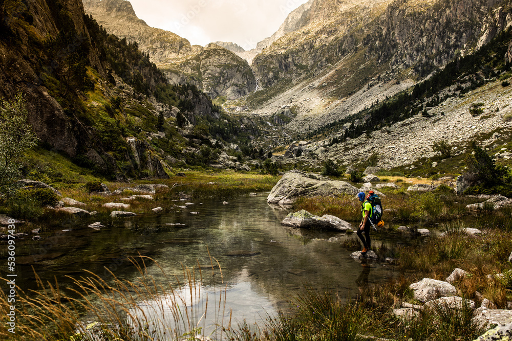 Backpacker crossing shallow mountain river Backpacker crossing shallow mountain river