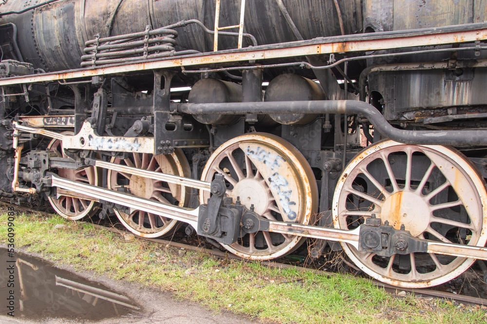 Drive transmission mechanism in a historic and damaged steam locomotive standing on a sidetrack. Rail.