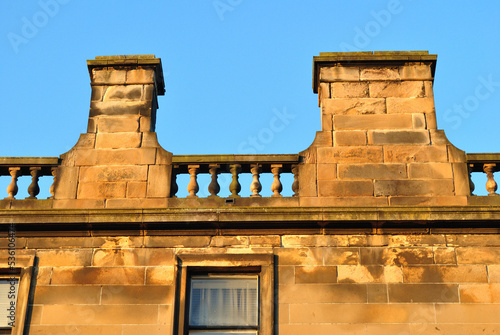 Fototapeta Weathered Stone Balustrade on Chimneys  on Old Stone Building against Blue Sky