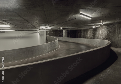 Way down to underground car parking. Perspective view of Curving shaped ramp of the basement made of concrete, Space for text, Selective focus.
