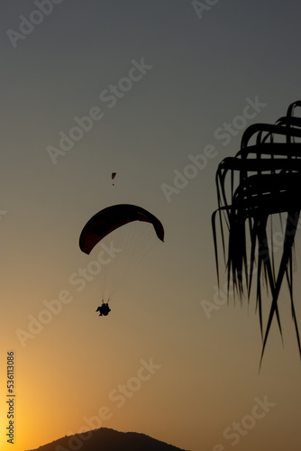Incredible sunset in Oludeniz with the landscape of the sea and the mountains, and silhouettes of people flying in paragliding.