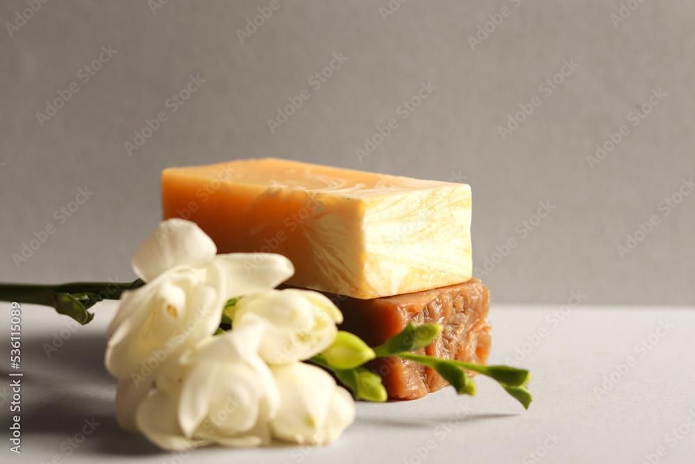Bars of natural soap on a gray background. Skincare cosmetic with branch of freesia flower. Beauty concept for body care. Bars of natural soap on a gray background. Skincare cosmetic with branch of freesia flower. Beauty concept for body care.