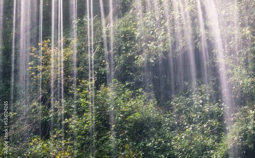 Long exposure of a view from behind a waterfall showing water dripping from the rock with trees in the background at Buttermilk Falls in Western Pennsylvania.