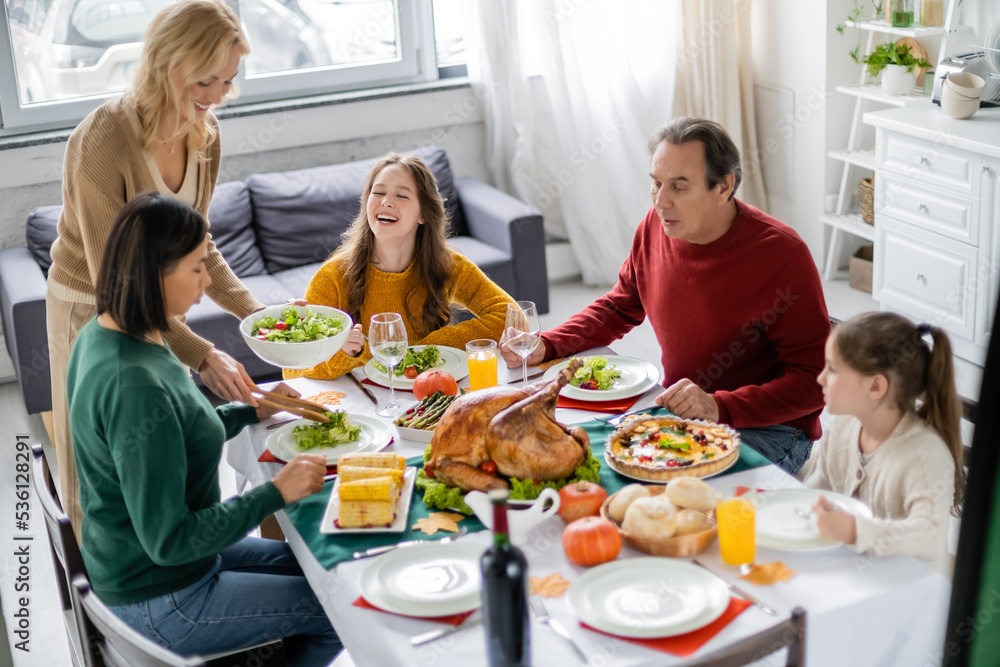Cheerful teenager sitting near multiethnic family and tasty thanksgiving dinner at home