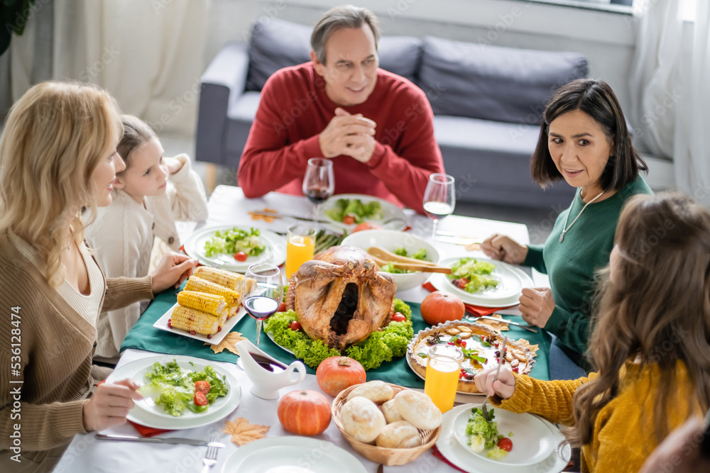 Interracial family talking near tasty thanksgiving dinner and drinks at home