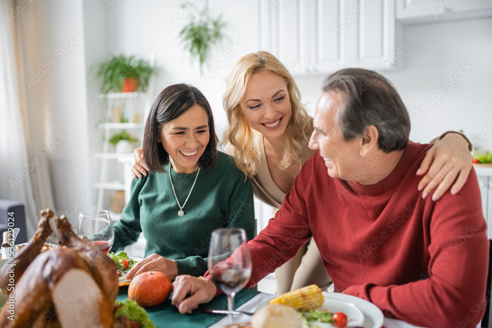 Positive woman hugging multiethnic parents near thanksgiving dinner at home