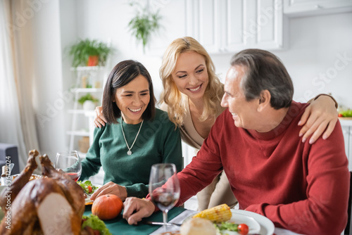 Positive woman hugging multiethnic parents near thanksgiving dinner at home
