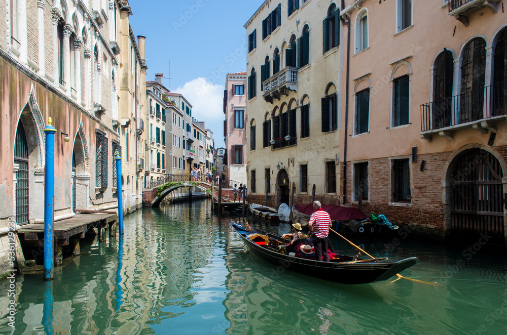 Una gondola naviga in un canale di Venezia in una giornata di sole guidata dal gondoliere con il vestito tradizionale