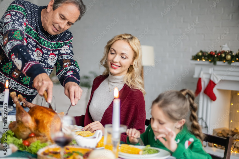 senior man cutting delicious roasted turkey during christmas dinner with happy family