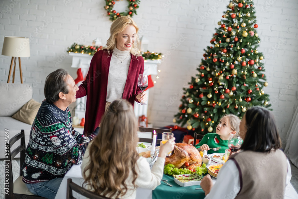 smiling woman toasting with glass of red wine during christmas dinner with interracial family smiling woman toasting with glass of red wine during christmas dinner with interracial family