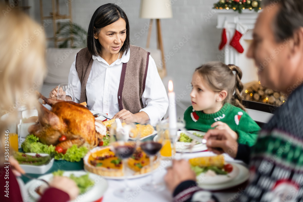 multiracial granny talking to granddaughter during christmas dinner with blurred family