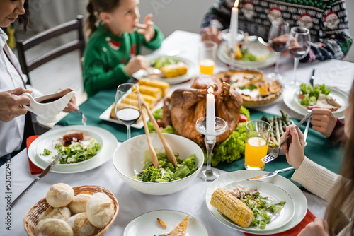 multiracial woman holding sauce boat near family having delicious thanksgiving dinner at home