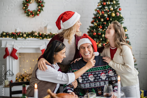 happy multiethnic family laughing near festive dinner and decorated christmas tree in living room