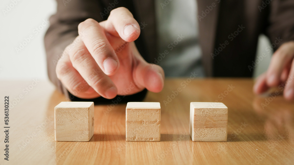 Businessman choosing a row of square wooden blocks on a wooden table. Business development concept and business decision. Businessman choosing a row of square wooden blocks on a wooden table. Business development concept and business decision.