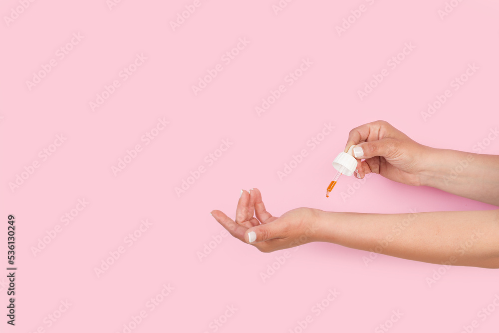 Mujer poniendose unas gotas de aceite esencial en la muñeca sobre un fondo rosa pastel. Vista de frente y de cerca. Copy space - obrazy, fototapety, plakaty 