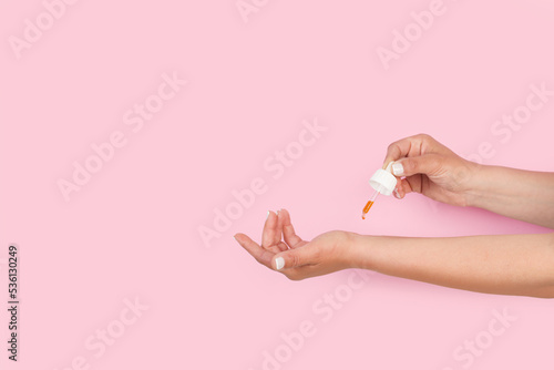Mujer poniendose unas gotas de aceite esencial en la muñeca sobre un fondo rosa pastel. Vista de frente y de cerca. Copy space photo