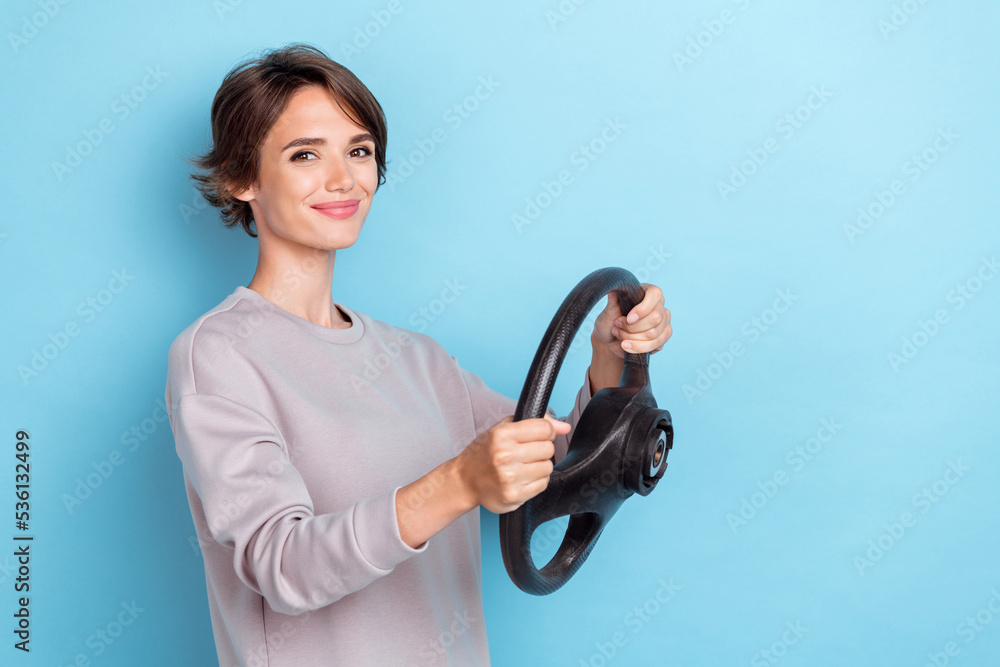 Portrait of optimistic girl with bob hairstyle wear gray pullover hold steering wheel driving license isolated on blue color background Portrait of optimistic girl with bob hairstyle wear gray pullover hold steering wheel driving license isolated on blue color background