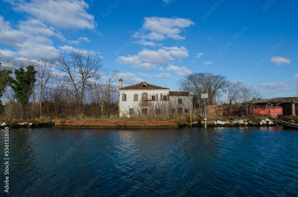 Una casa dell'isola di Mazzorbetto vista dal canale in una giornata di sole e nuvole Una casa dell'isola di Mazzorbetto vista dal canale in una giornata di sole e nuvole