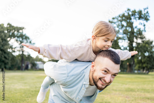 Father and little girl outdoors playing airplane and smiling.