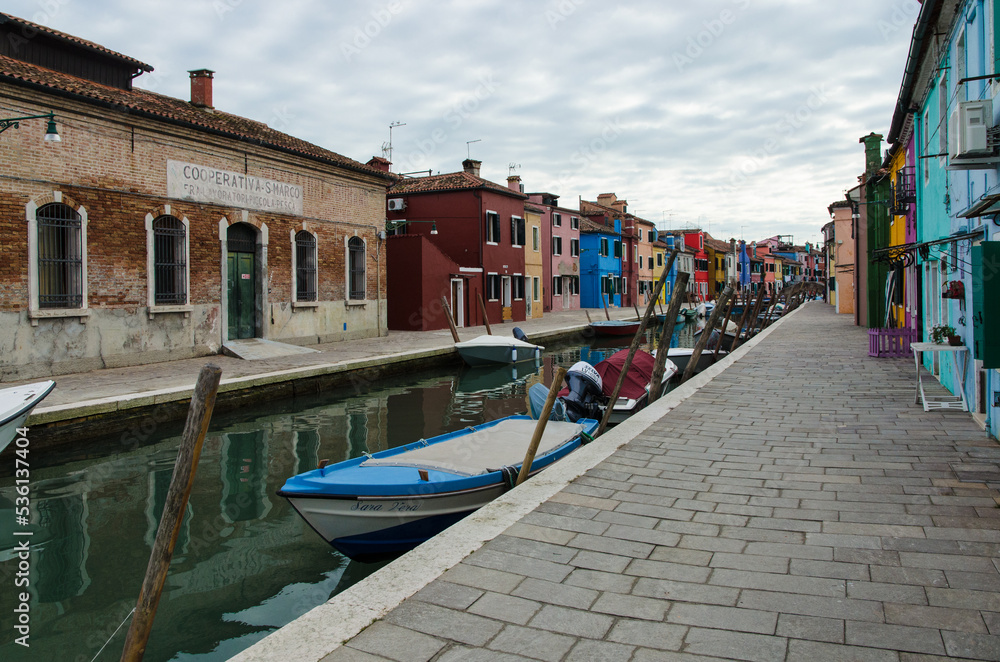 Barche ormeggiate in un canale di Burano con le tipiche case colorate in una giornata di sole con le nuvole 