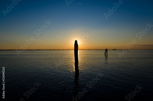 Il sole del tramonto si nasconde dietro una briccola, tipoco palo di segnalazione per la navigazione, a Burano, isola della laguna di Venezia photo