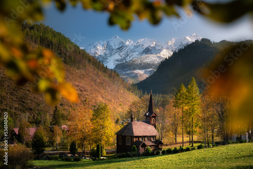 Autumn, view of the snow-capped Tatra Mountains and a wooden church, Slovakia. Jesień, widok na ośnieżone Tatry oraz drewniany kościół, Słowacja. Barwy jesieni pod Tatrami. 