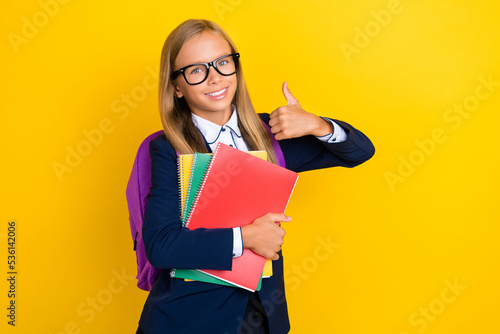 Photo of cheerful girl hand hold books rucksack satisfied lesson easy homework classroom empty space isolated on yellow color background