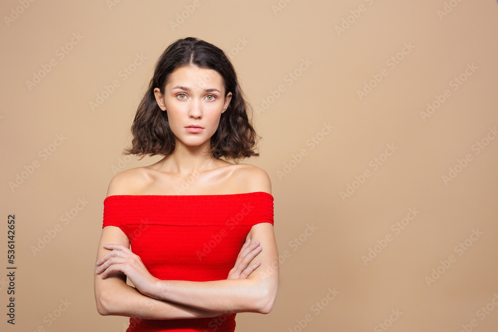sad woman with crossed arms on a beige background. a beautiful woman is tired and upset. emotions on the face. a young European woman for a sale poster, a place for text. closed posture, resentment sad woman with crossed arms on a beige background. a beautiful woman is tired and upset. emotions on the face. a young European woman for a sale poster, a place for text. closed posture, resentment