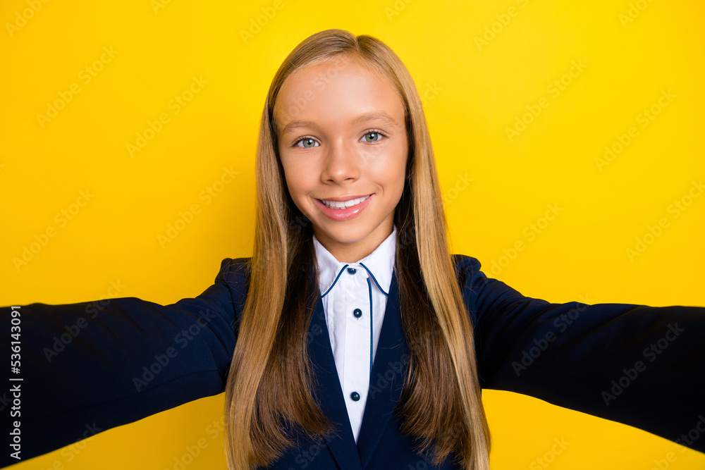 Portrait of positive cheerful cute schoolgirl with long hairstyle dressed blue jacket doing selfie isolated on yellow color background Portrait of positive cheerful cute schoolgirl with long hairstyle dressed blue jacket doing selfie isolated on yellow color background