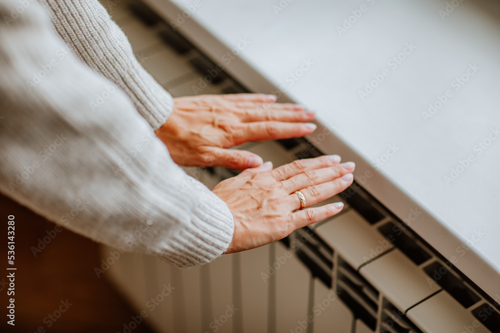 Obraz premium Woman's hands in winter sweater is touching home radiator and feeling cold