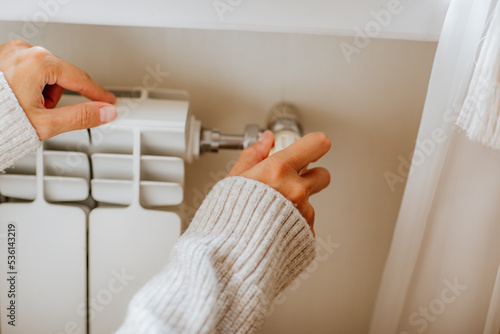 Woman's hands in long winter beige sweater is switching off home radiator