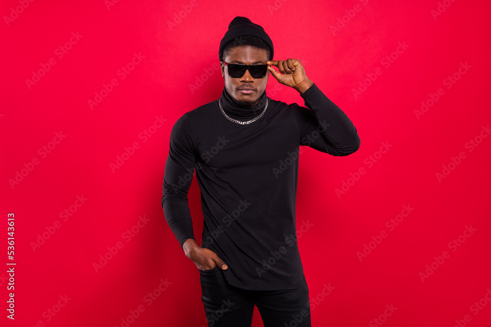 Portrait of attractive funky serious guy touching specs wearing black look isolated over bright red color background Portrait of attractive funky serious guy touching specs wearing black look isolated over bright red color background