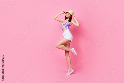 Full body portrait of cheerful excited lady hands touch panama hat stand tiptoe dance isolated on pink color background