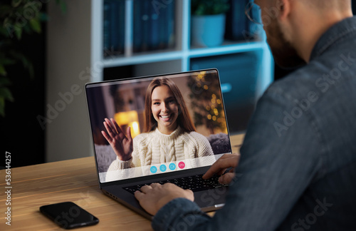 Man having video call with girlfriend at home, young cheerful lady waving by hand on the laptop screen