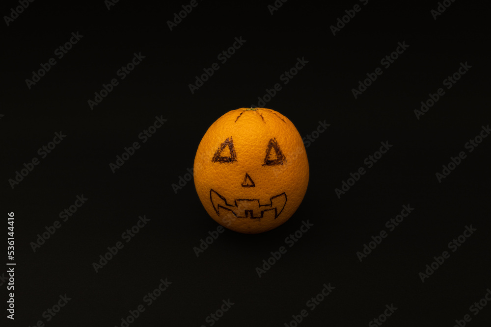 Orange looks like a Halloween pumpkin on a black background, scary fruit Orange looks like a Halloween pumpkin on a black background, scary fruit