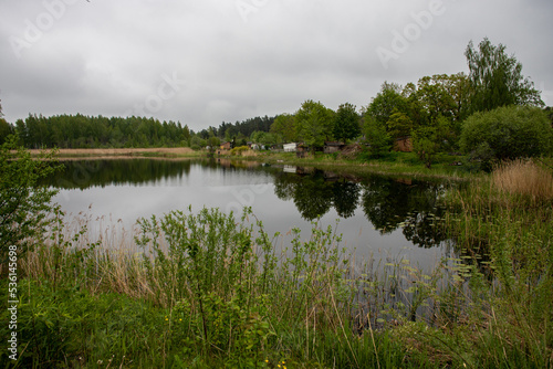 pond in Latvia countryside, reflection of trees and old lake side buildings