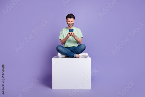 Full body photo of attractive young guy hold gadget sit white cube apple samsung wear trendy gray look isolated on violet color background