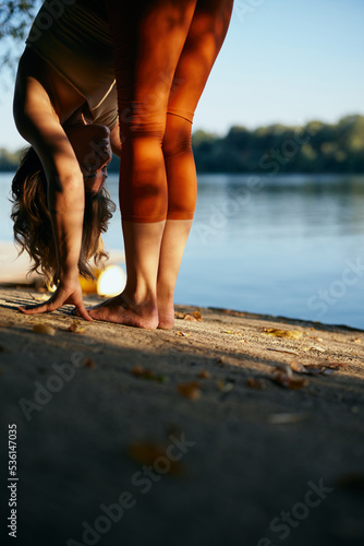 A slim yogi woman stretches and bends while practicing yoga in nature on the lake shore.