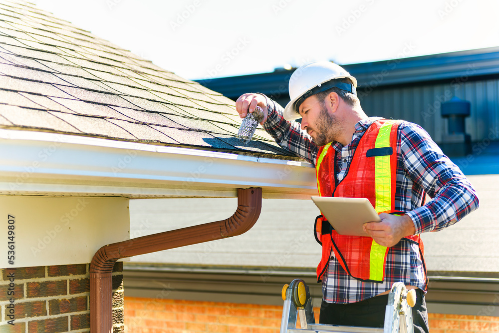 man with hard hat standing on steps inspecting house roof - obrazy, fototapety, plakaty 