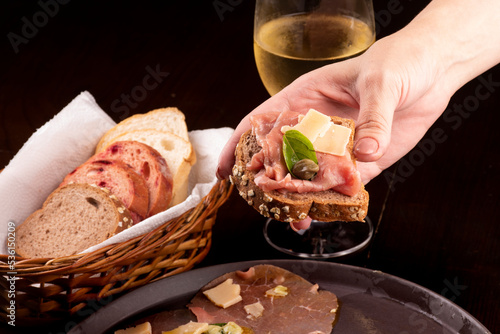 romantic dinner with carpaccio cold meat cattail basket of artisan breads glass of white wine female hand showing a canapé with caper photo