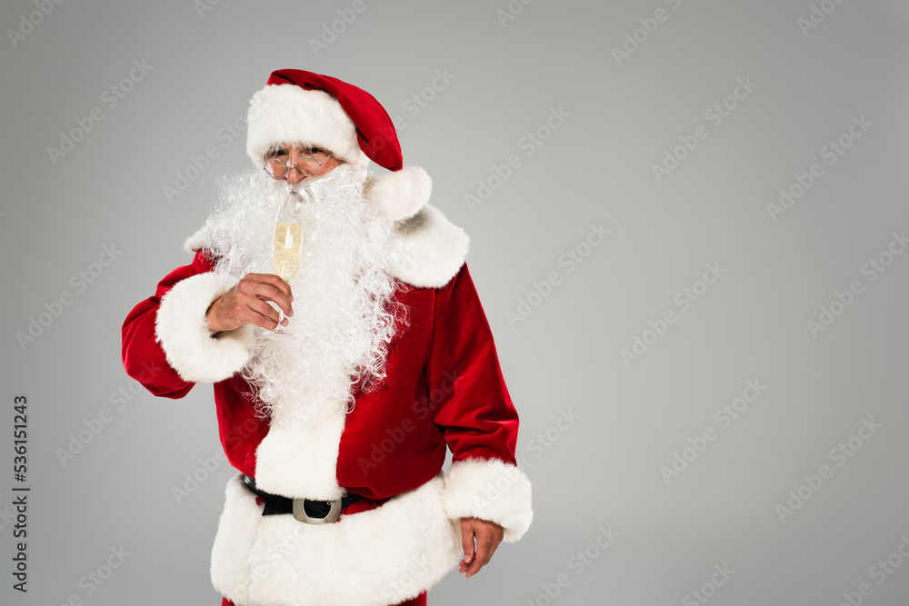 Santa claus in red costume holding champagne glass isolated on grey.