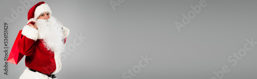 Santa claus in costume holding red shopping bag isolated on grey, banner. © LIGHTFIELD STUDIOS
