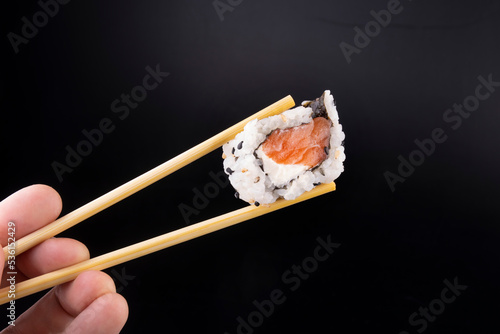 home made japanese food holding a salmon sushi with cream cheese with chopsticks isolated on black background macro close-up landscape fingers of hand